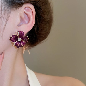 Gros plan d'une boucle d'oreille fleurie avec pétales violets et un grand cristal central