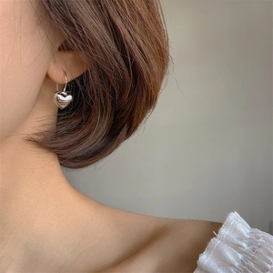 Minimalist 3D hollow heart drop earrings in polished silver on female model ear