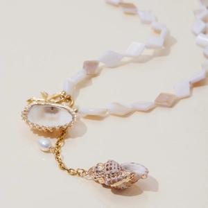 Macro detail of seashell necklace featuring white mother of pearl beads and conch pendant