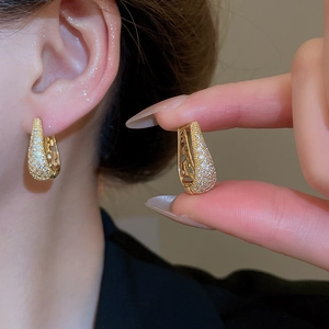 Gros plan de boucles d'oreilles en U dorées avec zircon et détails de cœur découpé