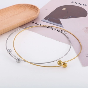 Close-up of gold and silver minimalist metal chokers with polished sphere ends on a tray