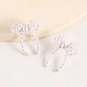 Close-up of handmade faux pearl bow earrings featuring woven beads and golden wire detail