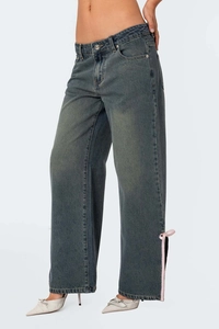 Détail de l'ourlet évasé avec nœud rose et fente latérale sur jean bleu gris foncé