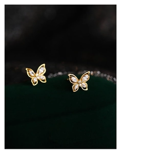 Macro shot of gold butterfly stud earrings with sparkling cubic zirconia on green velvet
