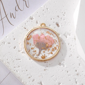 Round resin pendant featuring real pink dried daisy and gold leaf in copper frame
