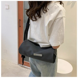 Sac bandoulière cylindrique gris foncé avec large sangle réglable porté sur le dos