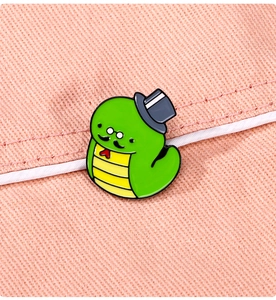 Macro shot of cute cartoon green snake enamel pin with top hat on pink fabric