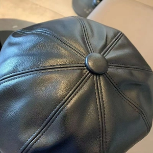 Close-up of black PU leather beret crown with center button and stitched panel details