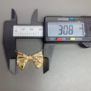 Close-up showing a 30.8 mm measurement of the gold bow pendant with colorful gemstones