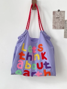 Detail of purple canvas tote with colorful tufted 'Let's think about earth' embroidery