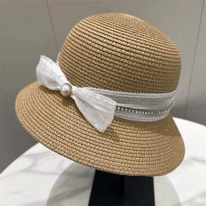 Elegant straw sun hat featuring a white lace bow and pearl accent on a minimalist stand
