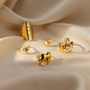 Set of five gold pearl rings with flower, heart, and eye motifs on beige silk background