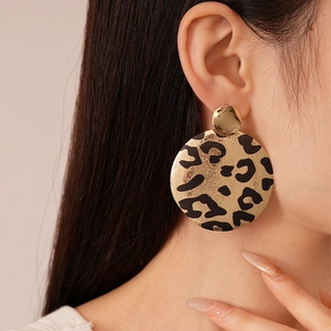 Gros plan de boucles d'oreilles rondes à motif léopard doré montrant le fini métallique chic