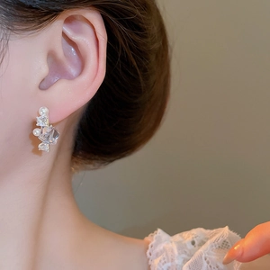 Close-up of zircon square crystal and pearl stud earring worn on model's ear