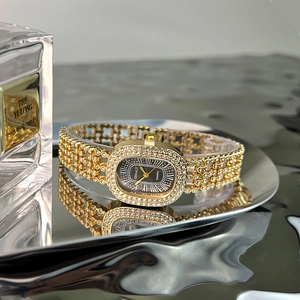Macro view of gold oval rhinestone watch with black Roman dial on a reflective tray
