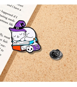 Macro view of magic cat enamel pin with purple wizard hat on books with back pin clasp