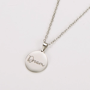 Macro view of silver stainless steel round pendant with engraved Dream script text