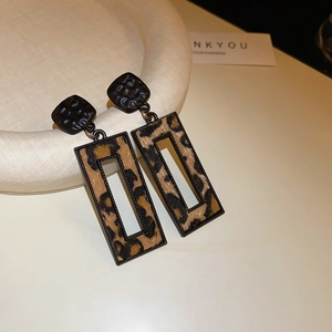 Detail view of rectangular leopard print earrings with matte black geometric studs on ceramic tray
