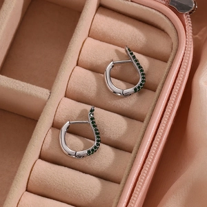 Macro detail of silver streamline earrings with green stones in a pink jewelry box