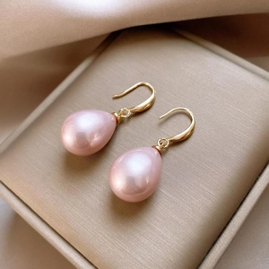 Elegant gold drop earrings with pink teardrop pearls presented on a jewelry cushion
