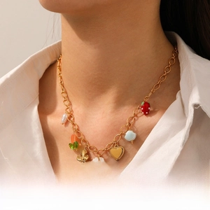 Détail d'un collier plaqué or avec breloques fraise et cœur porté par un mannequin
