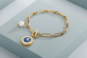 Detail of gold stainless steel bracelet with blue crystal and white pearl charms