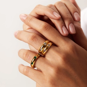 Close-up of chunky gold dome rings with green, white, and purple gemstones on hand