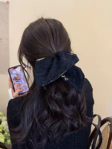 Detail of elegant black crepe bow hair tie with golden embroidery in a ponytail style