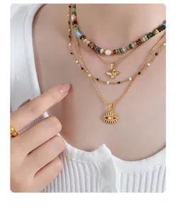 Detail of layered gold-plated necklaces with colorful beads and evil eye sun pendant