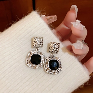 Detail of vintage silver square earrings with black gemstone on white knit fabric
