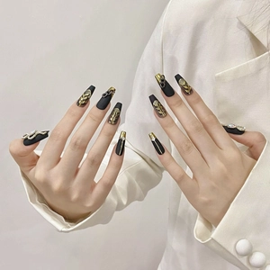 Handmade black matte coffin nails with gold leaves, chains, and crystals on a model hand