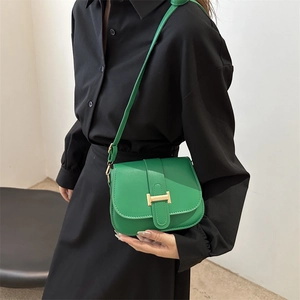 Green leather crossbody bag with golden H buckle shown on a model in a minimalist style
