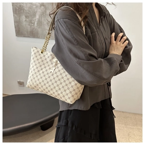 Detail view of cream tote bag with geometric print and gold deer charm on shoulder