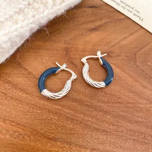 Minimalist silver and navy blue enamel twisted hoop earrings on a warm wooden background