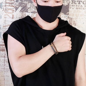 Close-up of stacked black leather rope and gold-tone chain bracelets worn by male model