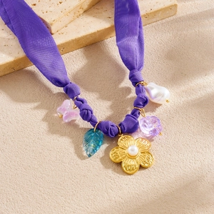 Detailed close-up of purple silk necklace with gold flower and butterfly charms