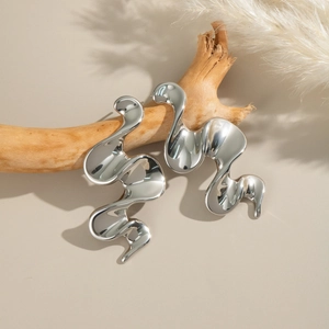 Detailed view of silver irregular wave earrings with metallic luster on wood decor