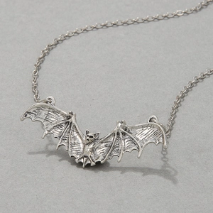 Macro shot of silver metal bat pendant with chain on textured gray background