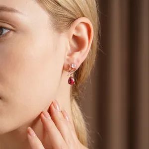 Elegant rose gold flower stud earrings with red teardrop crystal drops worn by model