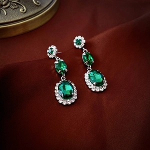Close-up of vintage emerald green oval earrings with crystal halo on red silk
