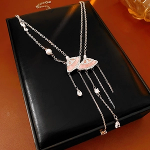 Detail of silver long necklace with pink fan pendants, tassels, and pearls on black box