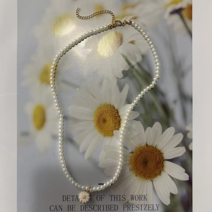 Detail of pearl necklace with daisy flower pendant and gold extension chain over floral art
