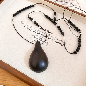 Macro shot of a black wooden teardrop pendant and beaded chain necklace on vintage paper
