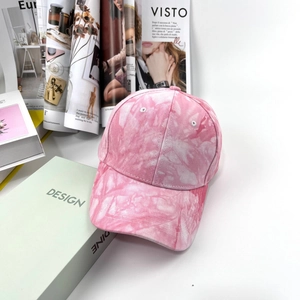 Dettaglio del berretto da baseball in cotone tie-dye rosa su sfondo di riviste