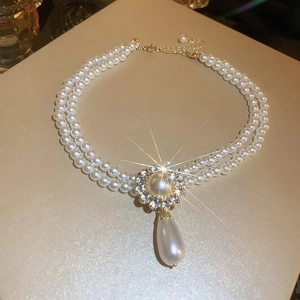 Double-layered pearl necklace with a gold diamond-rimmed pendant and droplet pearl charm