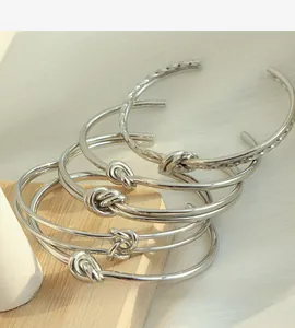 Dettaglio dei bracciali rigidi in acciaio al titanio argento con nodo intrecciato e forma a C
