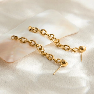 Detail of 18K gold-plated chain link drop earrings with spherical stud on pearlescent surface