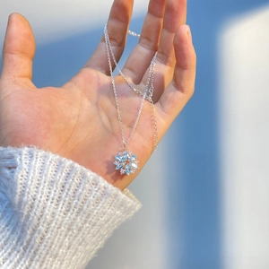 Elegant silver snowflake necklace with light blue stones held by hand on white sweater