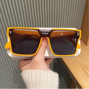 Handheld yellow square oversized sunglasses with dark lenses and FENG brand logo