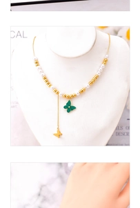 Detail of gold beads and white pearl necklace featuring green butterfly pendants on mannequin